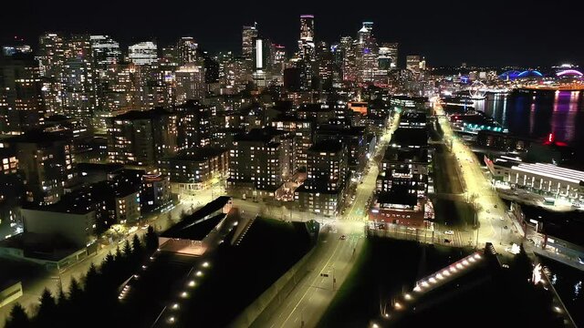 Cinematic 4K aerial, after sunset, night drone clip of downtown Seattle, Washington, Alaskan way waterfront with illuminated streets, offices looking from Elliott Bay Seattle Harbor during blue hour