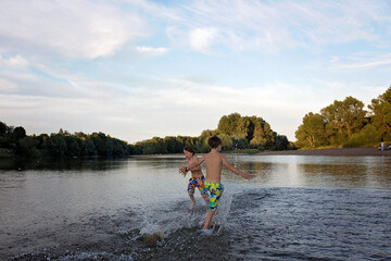 Fototapeta na wymiar Children, playing in a lake on sunset, swimming and running, splashing water, summertime