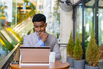 African businessman at coffee shop using laptop computer while thinking