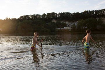Children, playing in a lake on sunset, swimming and running, splashing water, summertime
