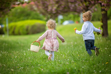 Fototapeta premium Beautiful children, toddler boy and girl, playing together in cherry blossom garden, running together and smiling with joy. Kids friendship