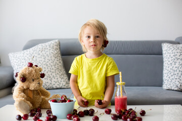 Toddler blond child, cute boy, eating cherries with teddy bears