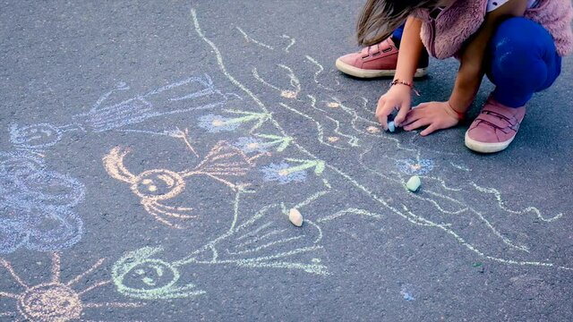 The child draws a family on the asphalt. Selective focus.