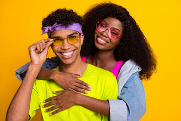 Portrait of attractive cheerful affectionate funky couple partners embracing isolated over bright yellow color background