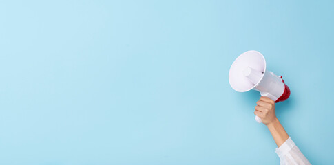 Business Hand holds a megaphone from a hole in the wall on blue background.  hiring, advertising,...