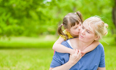 Fototapeta premium Little girl with special needs hugs and kisses her mother at summer park. Empty space for text