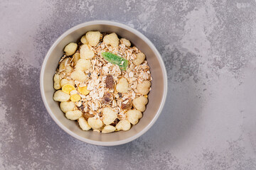 Fresh granola, muesli with coconut, banana and nuts in grey bowl on background.