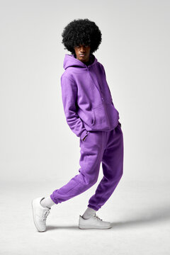 Young black man in set of purple tracksuit presenting white sneakers isolated on gray background