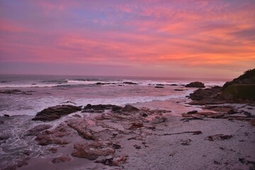 New Zealand, stunning sunset panorama in Catlins. Beautiful nature, beach with colorful red, orange and purple clouds reflected in the sea.