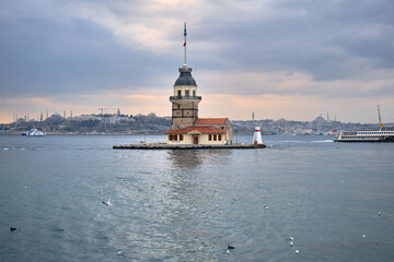 The maiden's tower (kiz kulesi) in stanbul, Turkey during overcast weather with sunshine reflection in bosporus sea.  Groups of seagulls flying on sea. stanbul Turkey 01.03.2021