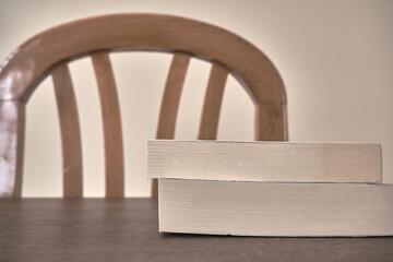 Wooden table and upper side of wooden  old, retro and vintage chairs with white wall background. Bundle of books stay on book.