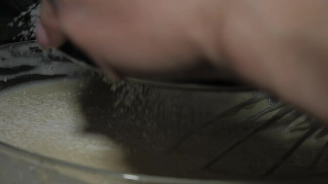 Skilled cook sifts flour over bowl with white pancakes dough holding sifter and whisk closeup. Restaurant nutrition