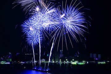 Stunning blue and white fireworks exploding into the night sky over the bay	