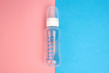 Pacifier and baby bottle on a blue and pink background.