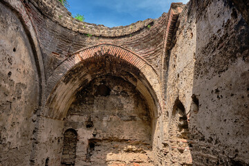 Old turkish bath ruins in iznik. It is established by ottoman empire period made of red bricks wall and currently it is abandoned and brownfield with demolished ist dome and blue sky is observed.