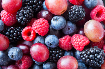 Background of fresh vegetables and fruits. Ripe blackberries, blueberries, plums, pink grapes, raspberries. Mix berries and fruits. Top view. Black-blue and red food.
