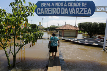 Fototapeta na wymiar People walk through a wooden footbridge set up above a flooded street in Careiro da Varzea, near Manaus (AM) during the rise of Negro River due to heavy rains in Brazil. The sign reads in Welcome.