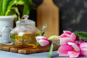 Fototapeta na wymiar green tea with rose petals in a transparent teapot on a wooden table on a black background. The background is blurred. Tea drinking.