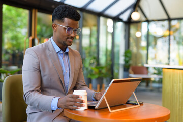 African businessman at cafe restaurant using laptop computer and holding coffee cup