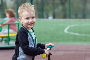 Cute caucasian boy with blue eyes and blond hair having fun at park children playground, with kick...