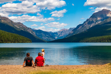family of three enjoying the calm blue waters of Bowmans lake and surrounding mountain range in Glacier National Park in Montana.
