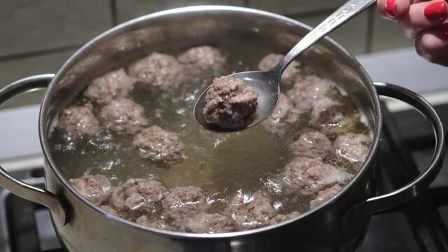 Women's hands stirring homemade bouillon with meatballs. Preparation of meatball soup. Close-up. Selective focus