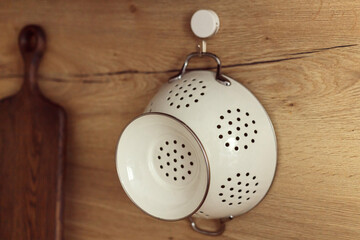Metal white colander hanged on hook on a kitchen wooden wall. - obrazy, fototapety, plakaty