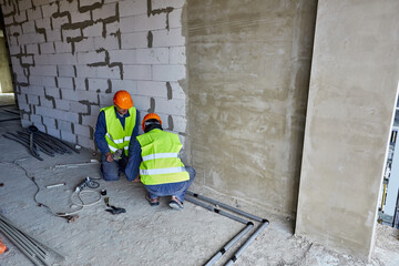 Two workers or builders in protective clothing and orange hard hats installing plastic pipes using...