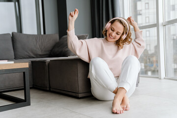 White woman listening music with headphones while sitting on floor