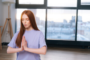 Close-up of redhead focused young woman meditating sitting on floor in lotus pose, Namaste mudra in...