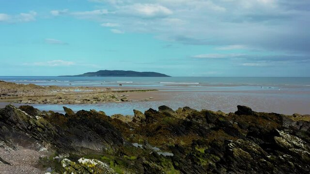 Aerial low view of drone flying over rocky beach landscape and revealing the Irish sea and Lambay Island.  Donabate beach in summer, Dublin, Ireland