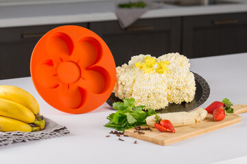 round orange silicone mold for baking, pastries or cakes, next to fruits and herbs, on a white...