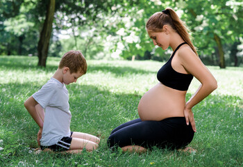 Pregnant woman sits in yoga posies and meditates with her son.