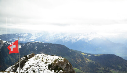 Swiss alps from Leysin mountain with Swiss flag pole on a cloudy day
