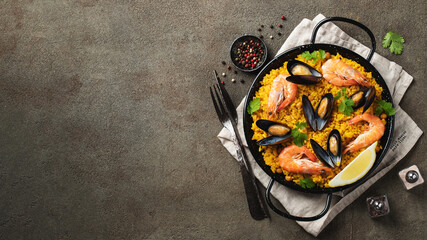 Traditional spanish seafood paella in pan with chickpeas, shrimps, mussels, squid on brown concrete background. Top view with copy space. Banner