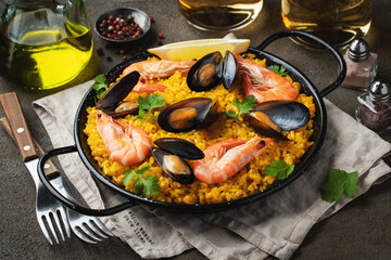 Traditional spanish seafood paella in pan with chickpeas, shrimps, mussels, squid on brown concrete background.