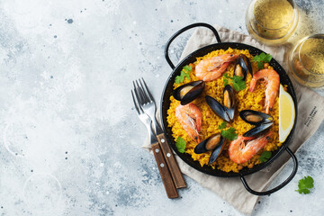 Traditional spanish seafood paella in pan with chickpeas, shrimps, mussels, squid on light grey concrete background. Top view with copy space