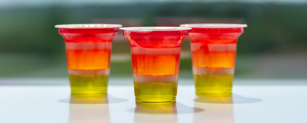 Three glasses of colorful striped jelly on a natural background. Rainbow jelly for kids party. Close-up.