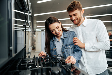 Young couple choosing new gas stove in home appliances store