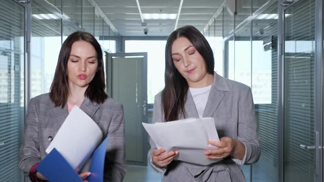 Lady busy financial director in grey jacket talks to manager and gives report sheets of papers walking along office building hallway close view