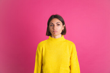 Beautiful woman in bright yellow sweater isolated on pink background look to camera with unhappy sad disappointed face