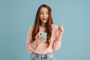 Young ginger woman pointing finger upward while using mobile phone