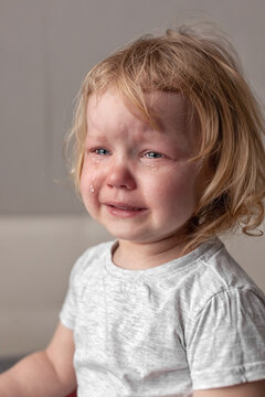 picture frustrated toddler in gray T-shirt with shoulder-length blond hair and tears on his cheeks