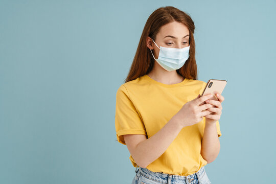 Young ginger white woman in face mask using mobile phone