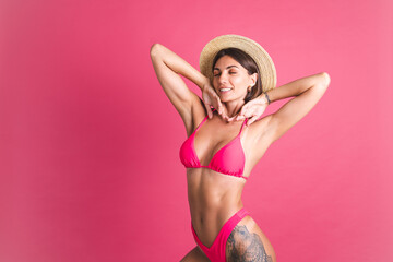 Beautiful fit tanned sporty woman in bikini and straw hat on pink background