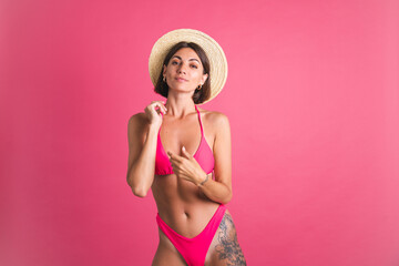 Beautiful fit tanned sporty woman in bikini and straw hat on pink background