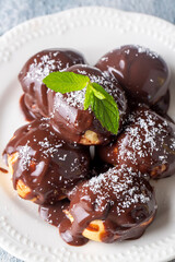 Delicious profiteroles with chocolate and white plate. Selective focus image on light background.