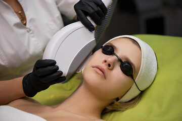 Therapist beautician makes a laser treatment to young woman's fa
