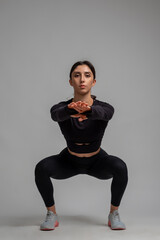 Sporty young woman doing squats on grey background
