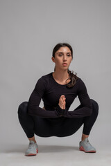 Focused girl doing stretching squats on grey background